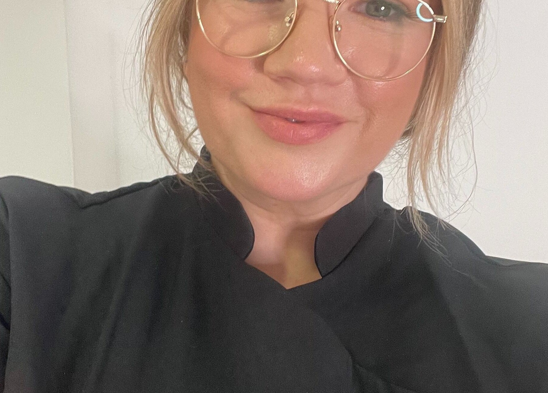 Expert beautician at BARE FACED, Worsley, England, GB in a professional black uniform and glasses, smiling.
