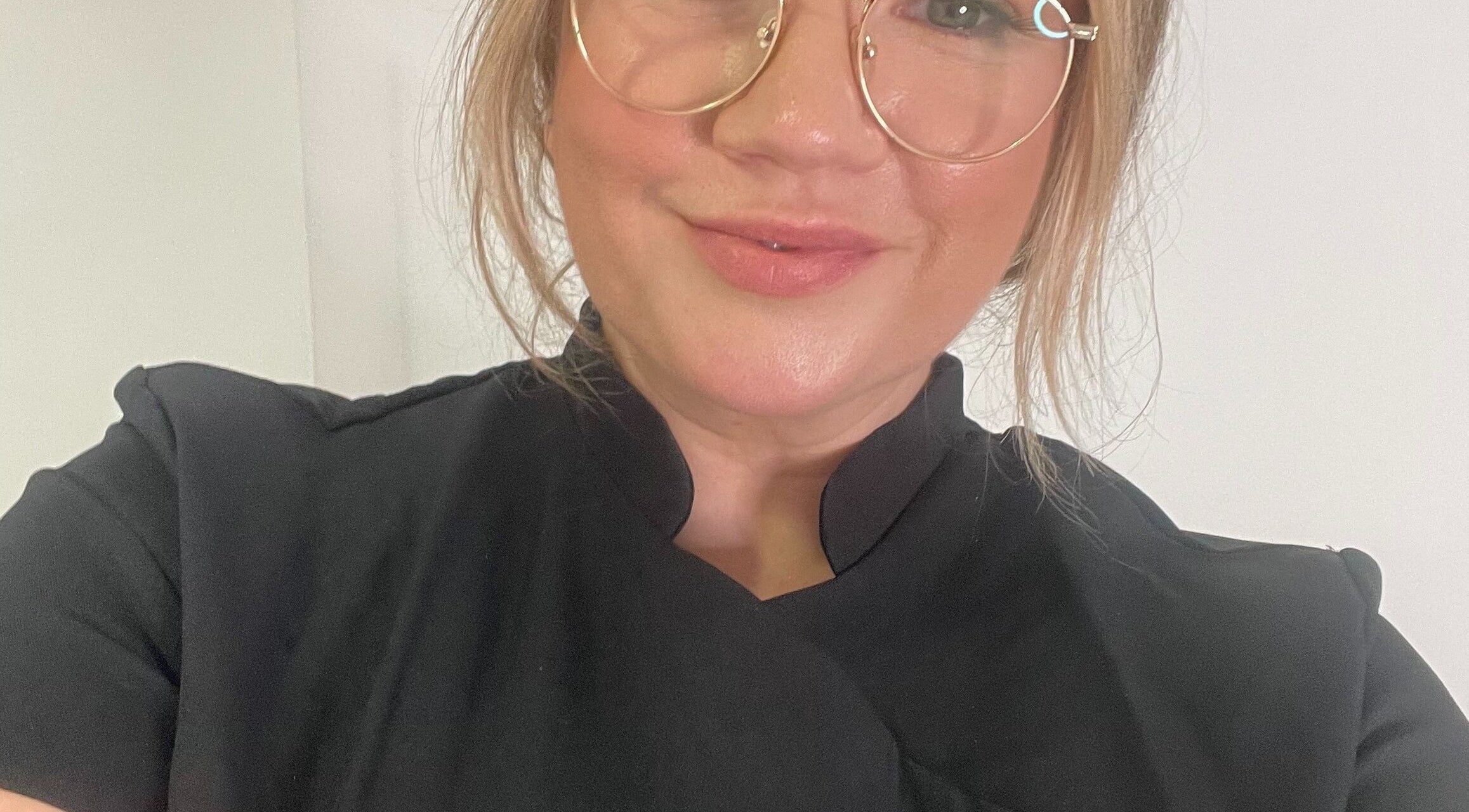 Expert beautician at BARE FACED, Worsley, England, GB in a professional black uniform and glasses, smiling.