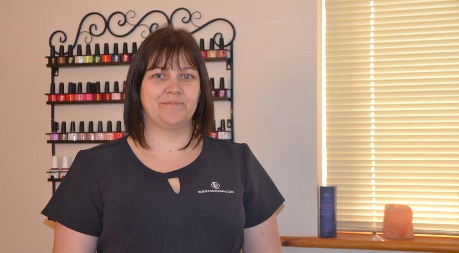 Staff member at La Belle Vita Wellness, Rye, England, standing by colorful nail polish display.
