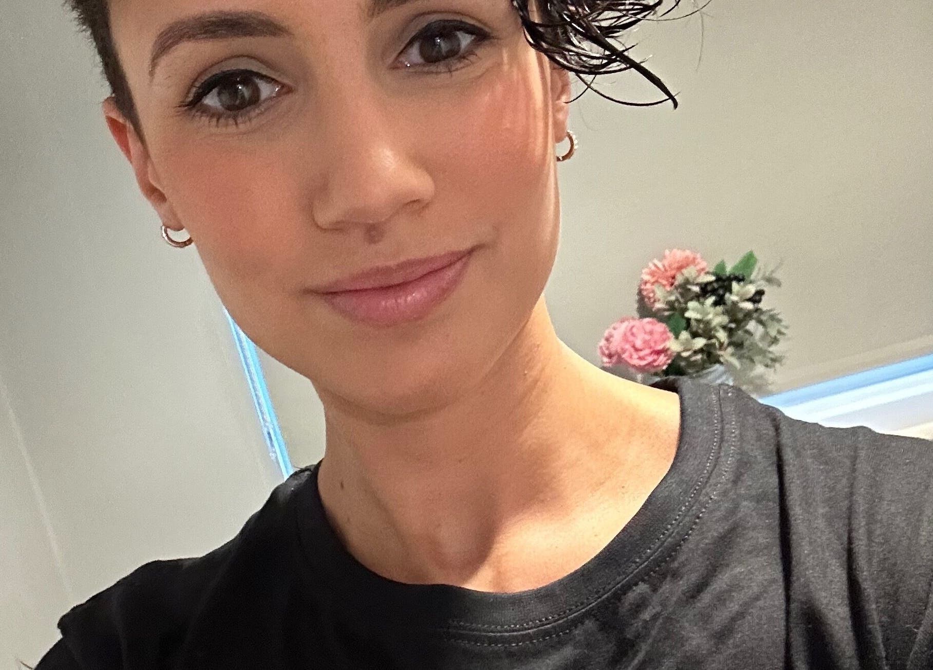 A person smiling in a cozy room at Wellness With Sophia, Stamford, England, GB, with flowers in the background.