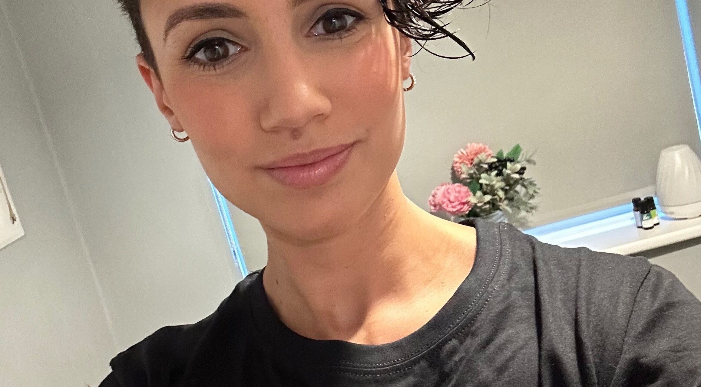 A person smiling in a cozy room at Wellness With Sophia, Stamford, England, GB, with flowers in the background.