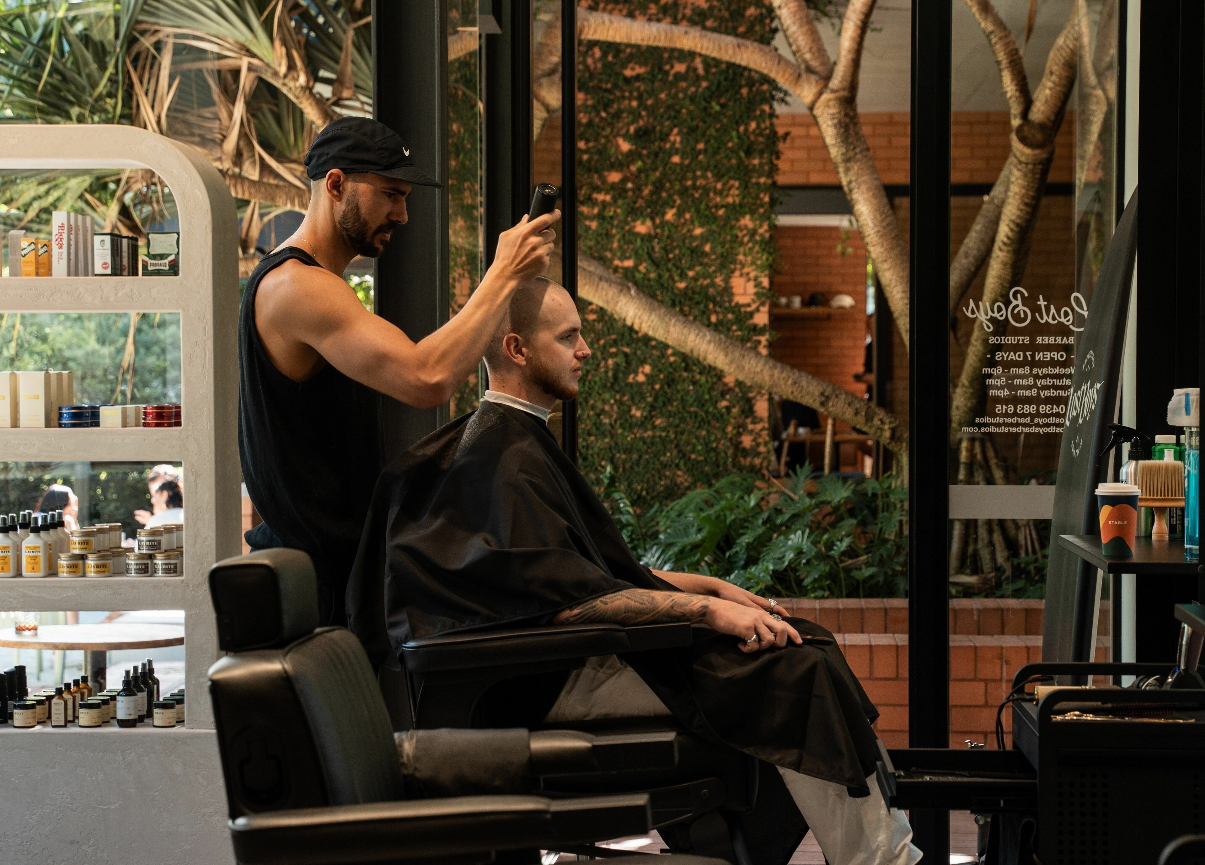 Stylist cutting hair at Lost Boys Tugun, in serene Tugun, Queensland, AU amidst lush green backdrop.