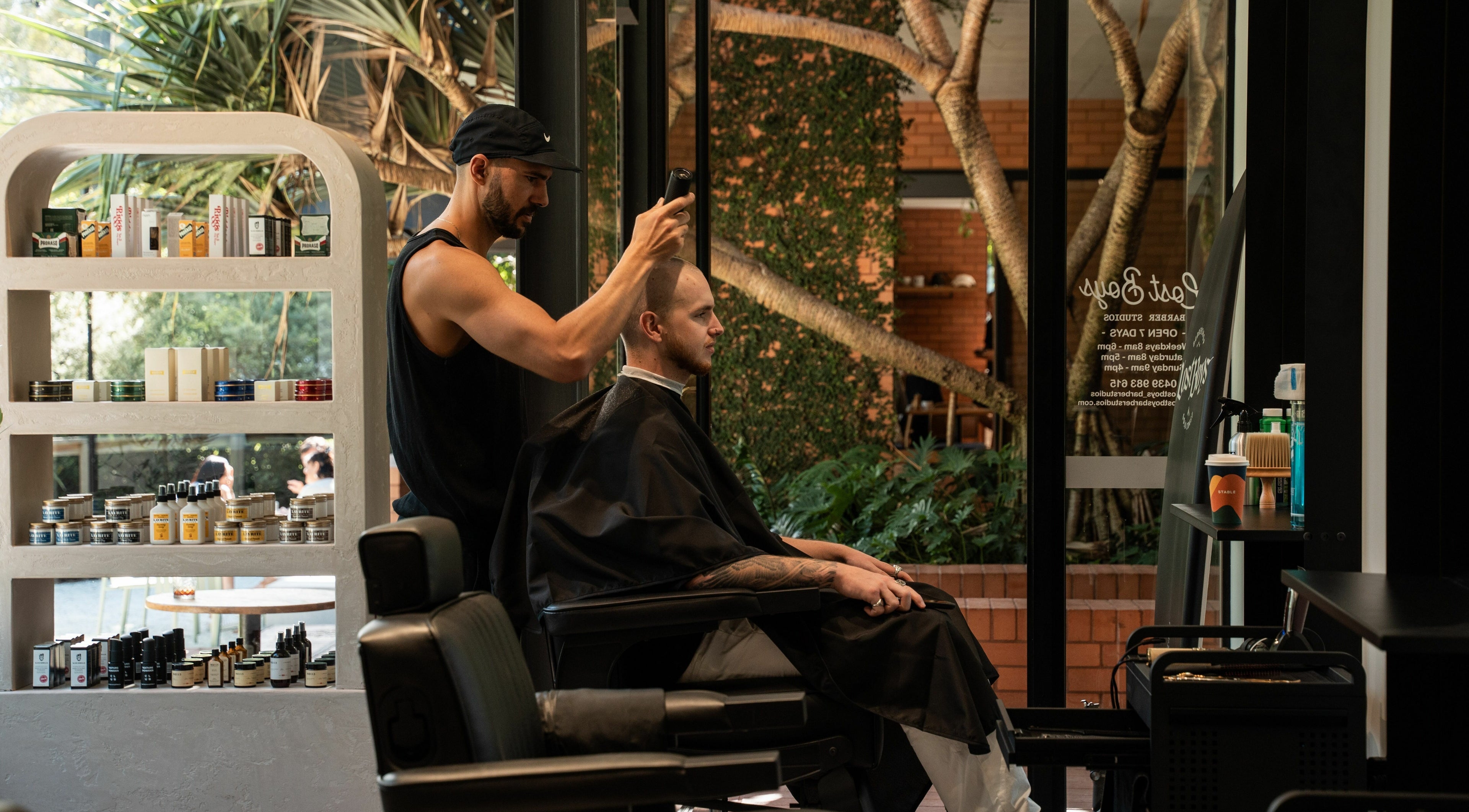 Stylist cutting hair at Lost Boys Tugun, in serene Tugun, Queensland, AU amidst lush green backdrop.