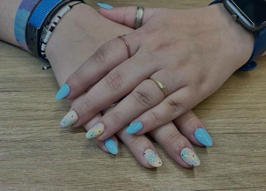 Stylish blue and floral nails by Jeweled by Jules in Ottawa, Ontario, CA displayed on a wooden surface.
