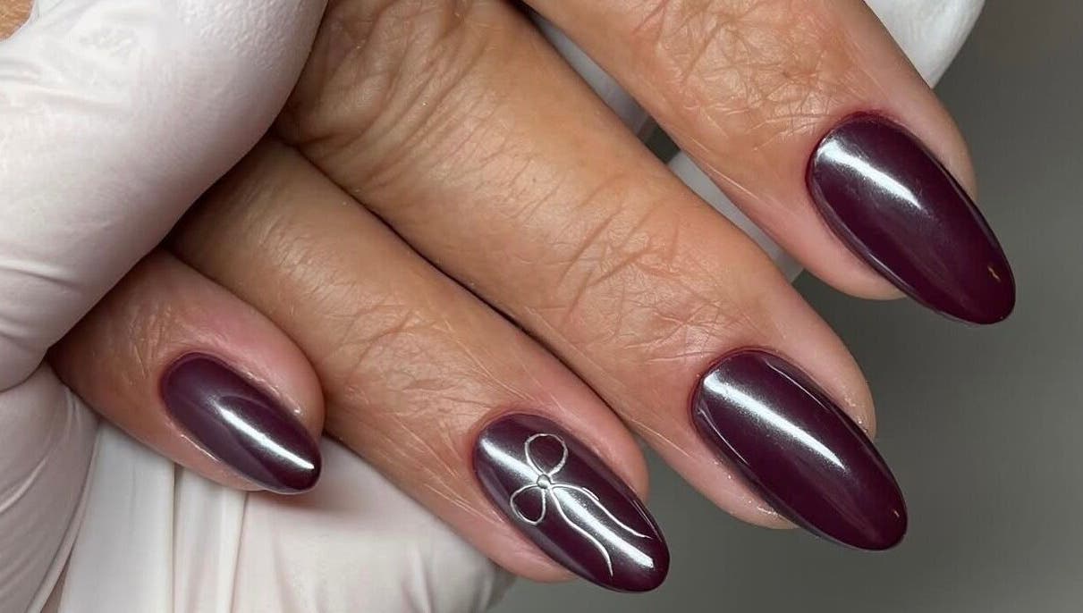 Elegant burgundy nails with delicate bow design at Mbm Nails, Hadleigh, England, GB.