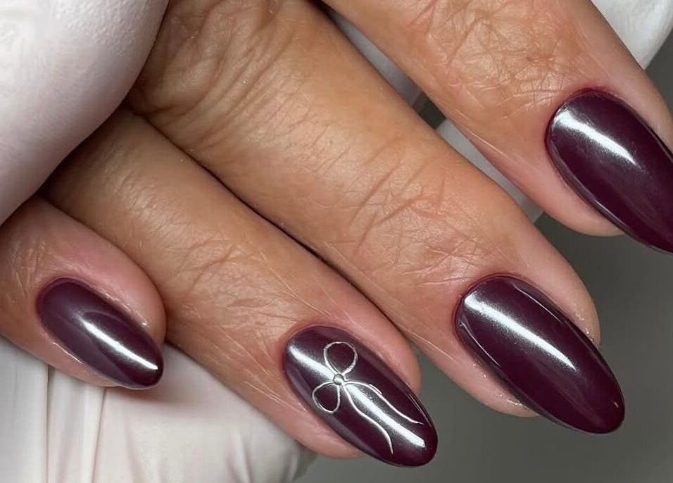 Elegant burgundy nails with delicate bow design at Mbm Nails, Hadleigh, England, GB.