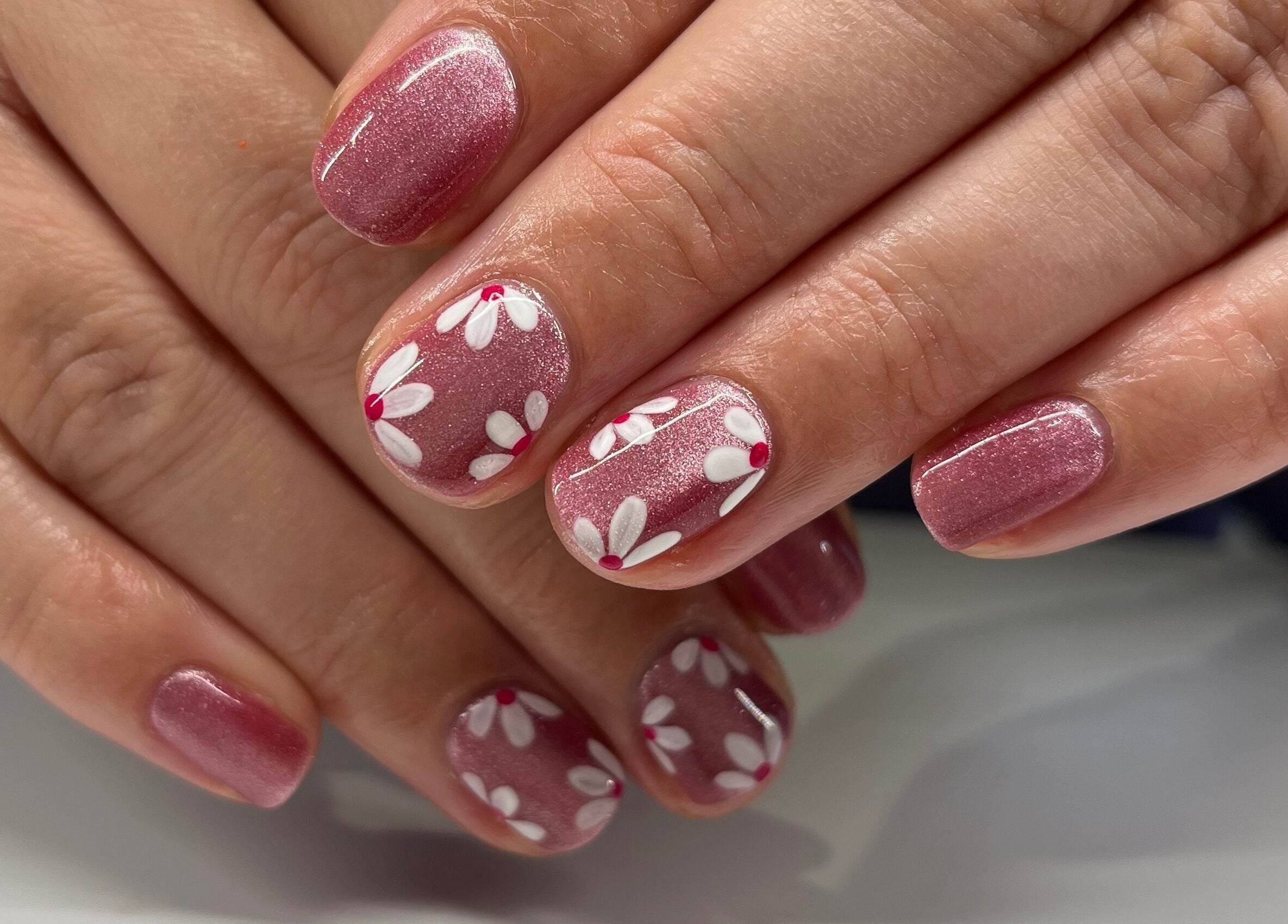 Elegant floral nail art at The Beauty Shed, West, England, GB. Features pink nails with white flower designs.