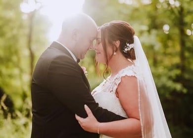 Couple embracing at JOAM Glow London Mobile Spray Tanning Sienna X, London, England, GB amidst lush greenery.