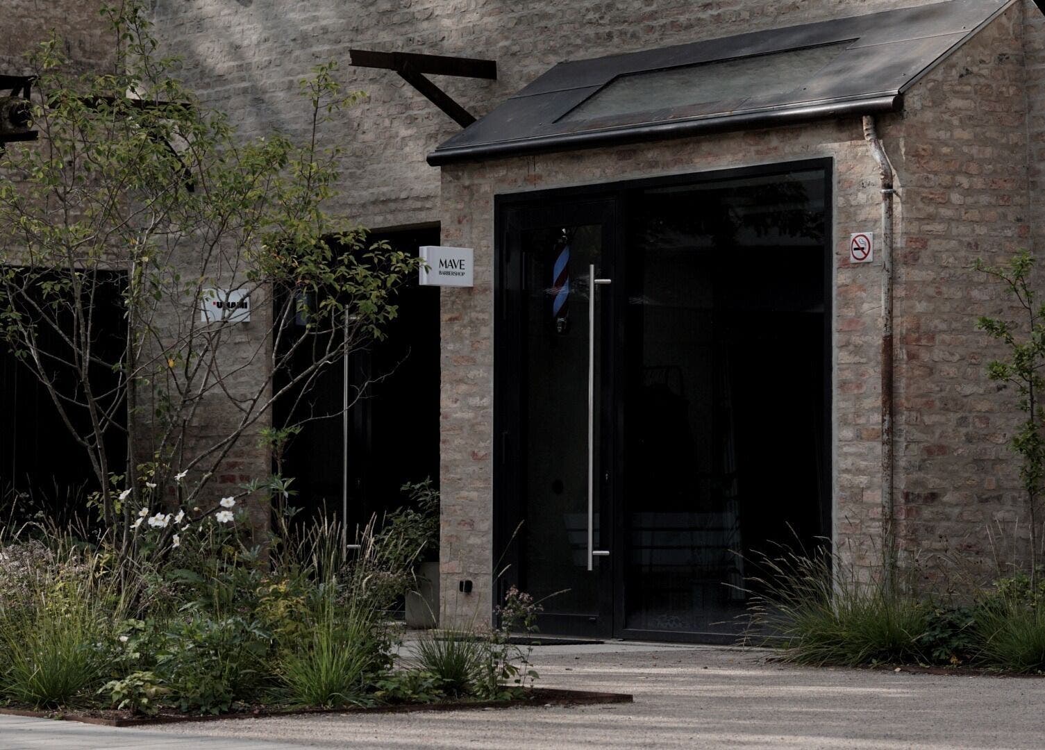 Entrance of Mave Barbershop | A.BRIĀNA in Rīga, LV with rustic brick facade and greenery.