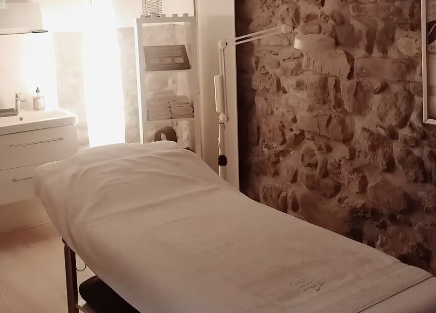 Salle de soin apaisante à Lumin'Essences, Lutry, Vaud, CH avec murs en pierre et table de massage.
