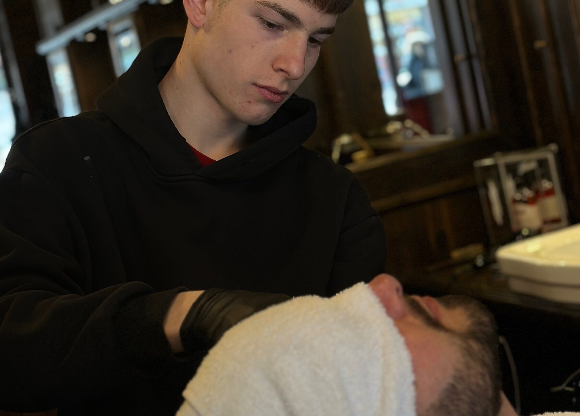 Barbiere a Peloloco Tiburtina, Roma, Lazio, IT, applica asciugamano caldo su cliente durante rasatura.