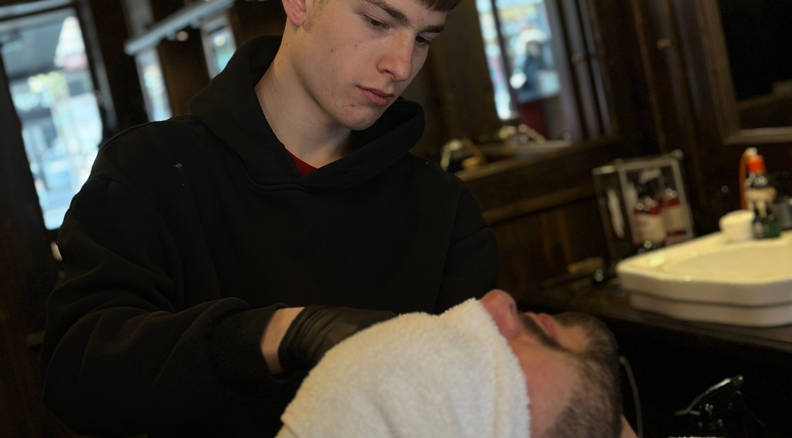 Barbiere a Peloloco Tiburtina, Roma, Lazio, IT, applica asciugamano caldo su cliente durante rasatura.