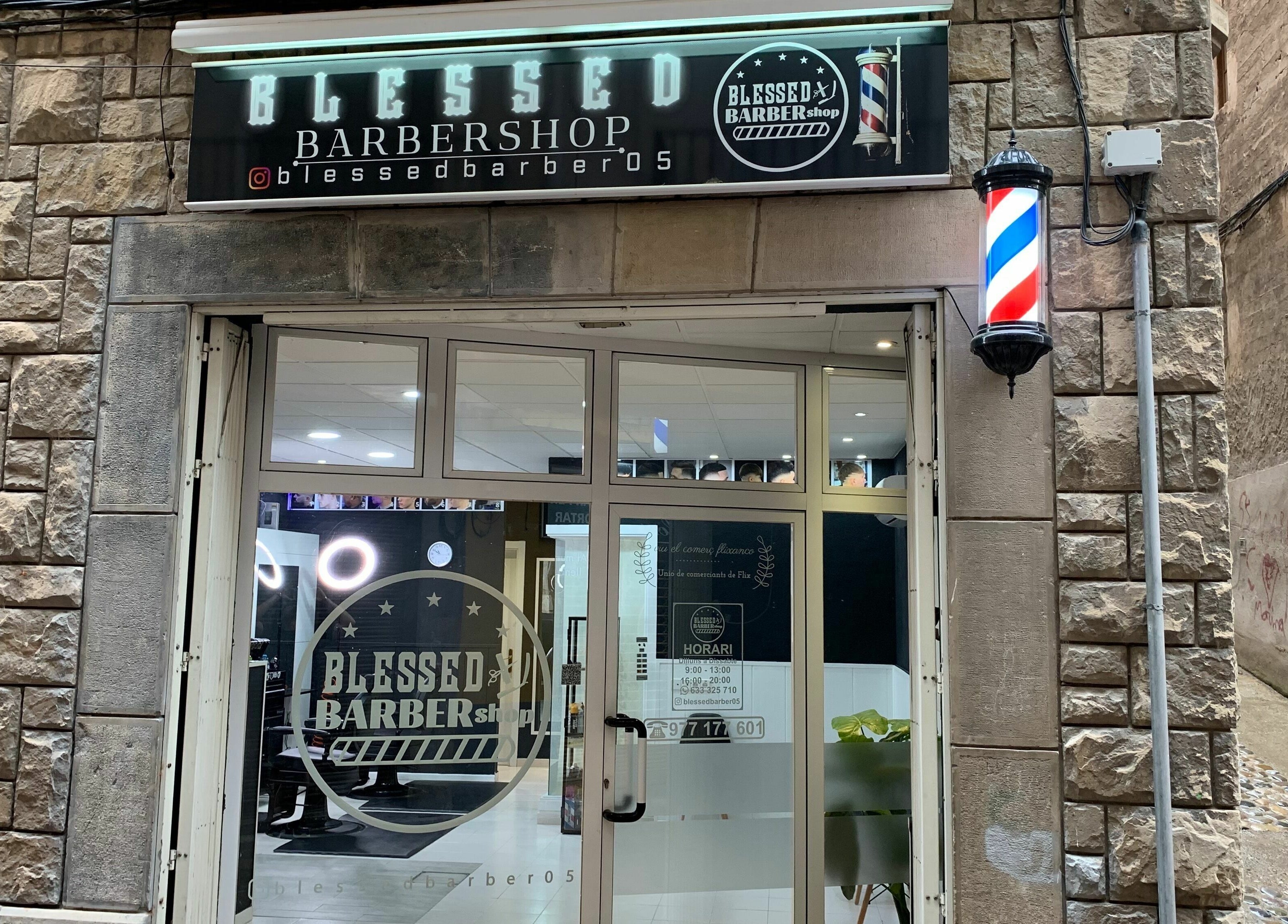 Entrada iluminada de Blessed BarberShop en Flix, Catalunya, ES con letrero y poste clásico.