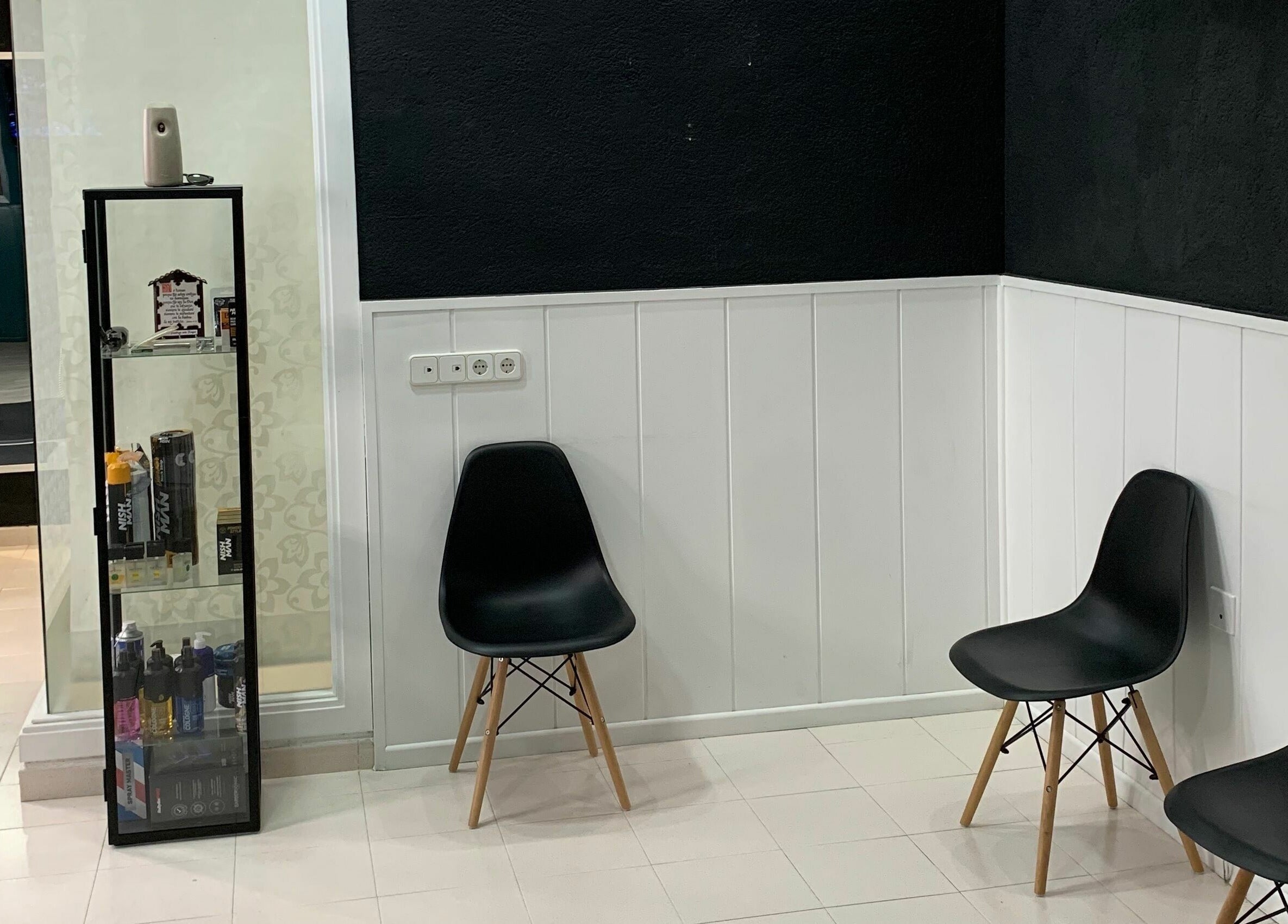Área de espera moderna en Blessed BarberShop, Flix, Catalunya, ES con sillas negras y estante de productos.