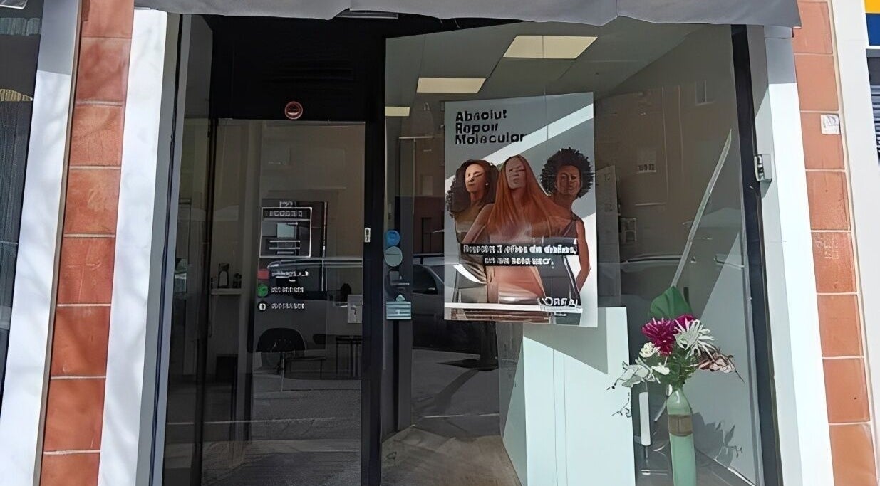 Entrada de Esencia Hair Salon en Granollers, Catalunya, ES con un afiche llamativo y flores en el escaparate.