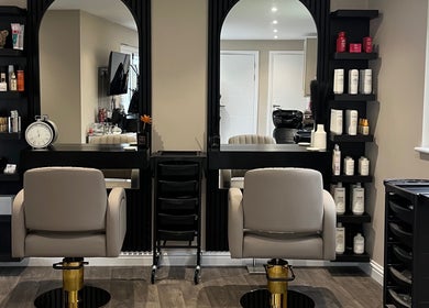 Elegant salon workspace at Hair by Tia, Stanway, England, GB with modern chairs and shelves of beauty products.