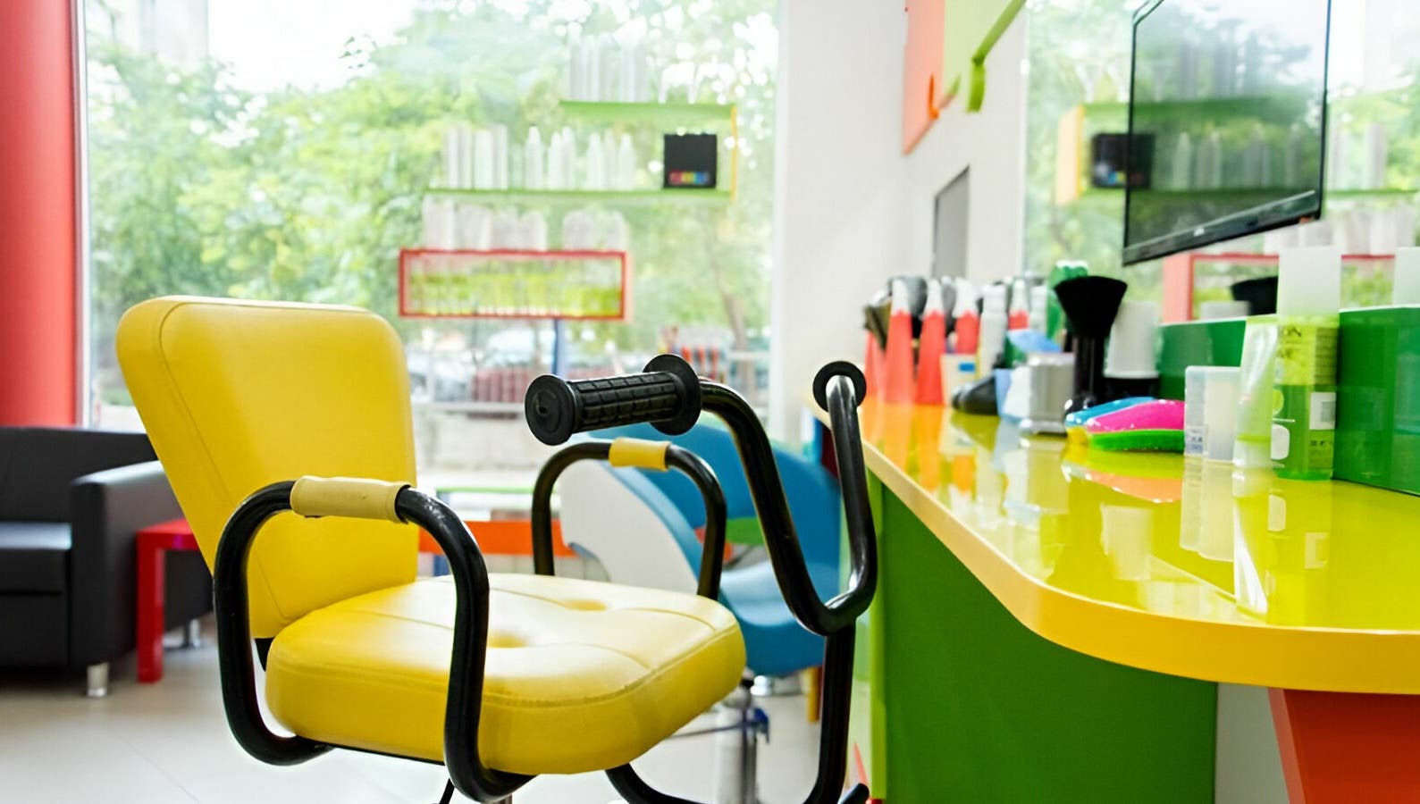 Ярко жълт фризьорски стол в ПЪЗЕЛ София кв. Гео Милев, София, BG, с цветни козметични продукти на преден план.