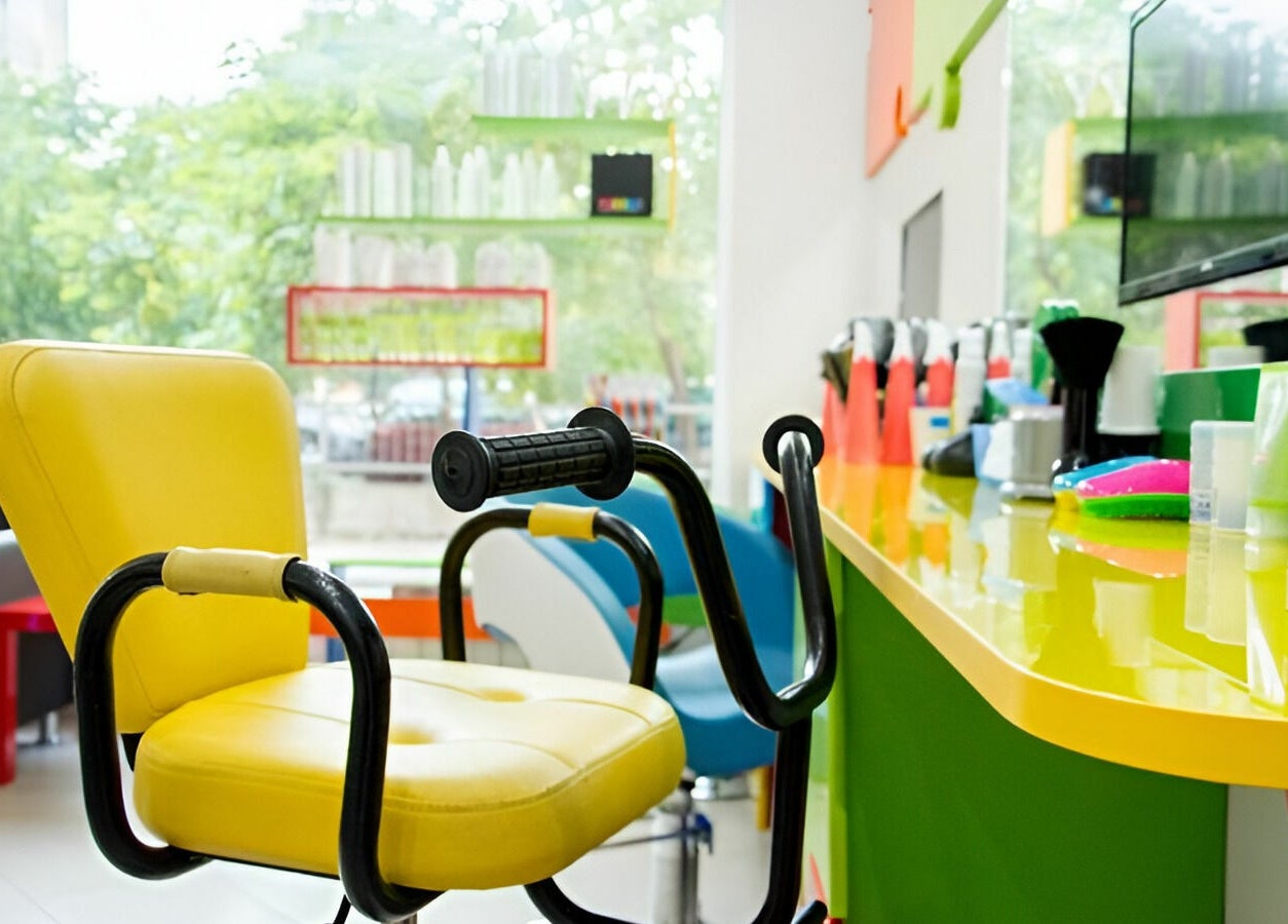Ярко жълт фризьорски стол в ПЪЗЕЛ София кв. Гео Милев, София, BG, с цветни козметични продукти на преден план.