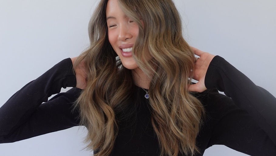 Smiling woman with wavy hair styled at Estrella Salon, San Diego, California, US.