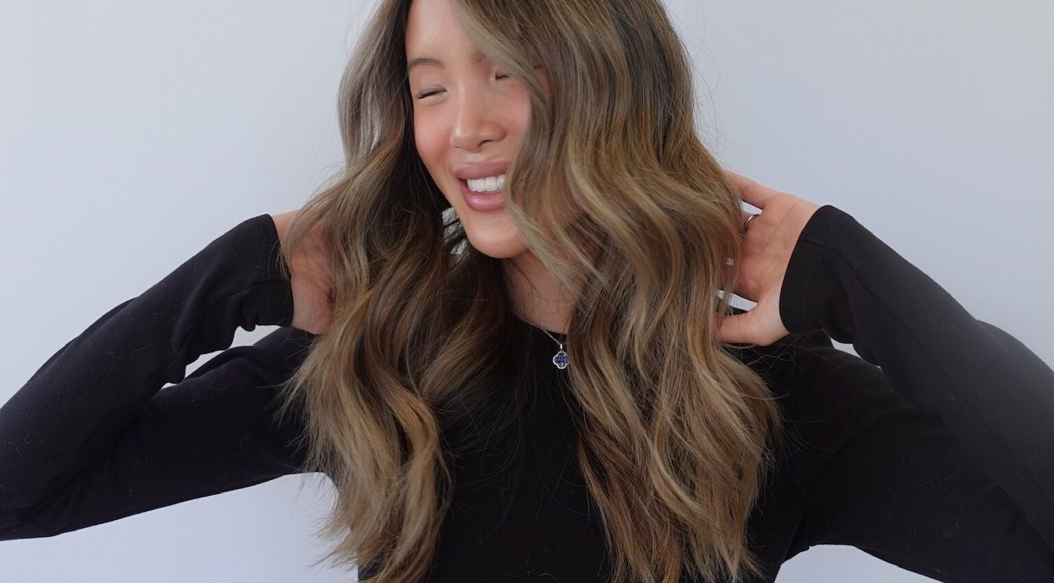 Smiling woman with wavy hair styled at Estrella Salon, San Diego, California, US.