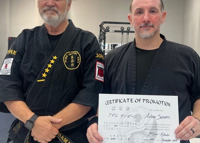 Martial arts instructors at Warrior’s Edge in Dallas, Texas, US, showcasing a promotion certificate.