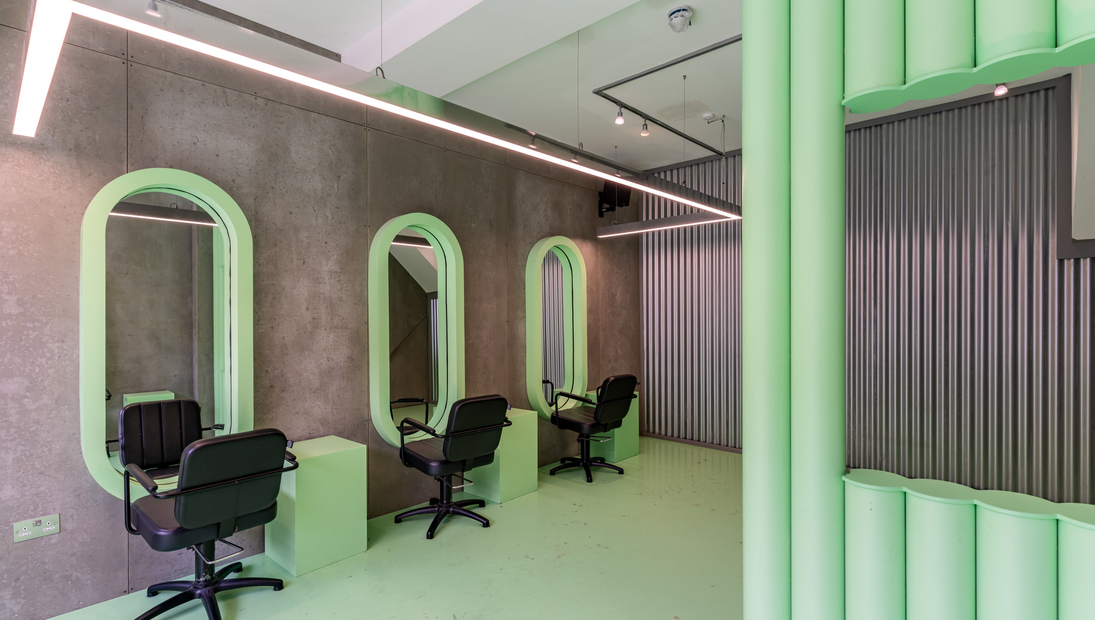 Modern salon interior with green accents at Crab Salad Highbury in London, GB features chic styling stations.