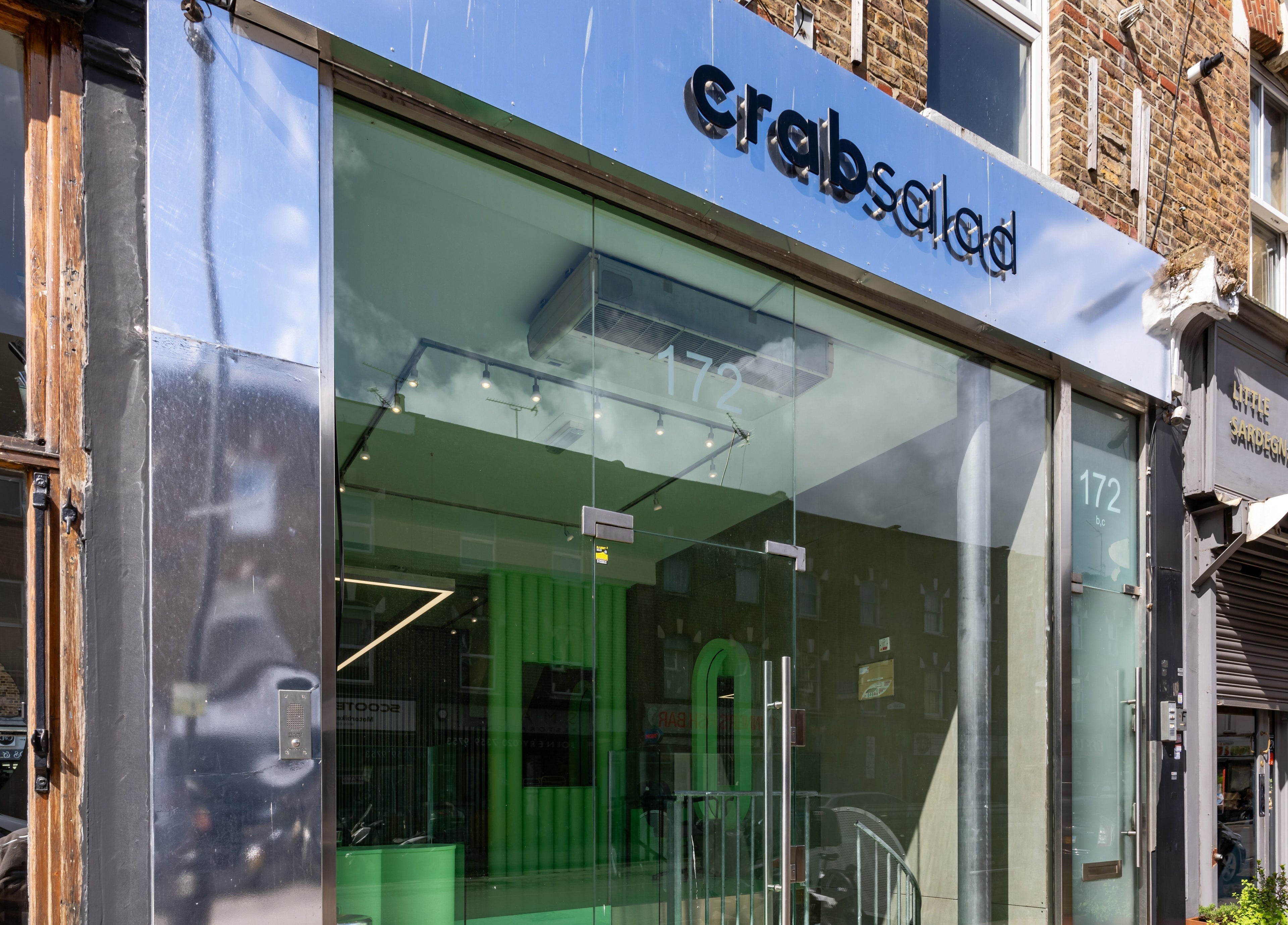 Front view of Crab Salad Highbury in London, GB, showcasing a sleek glass entrance with modern signage.