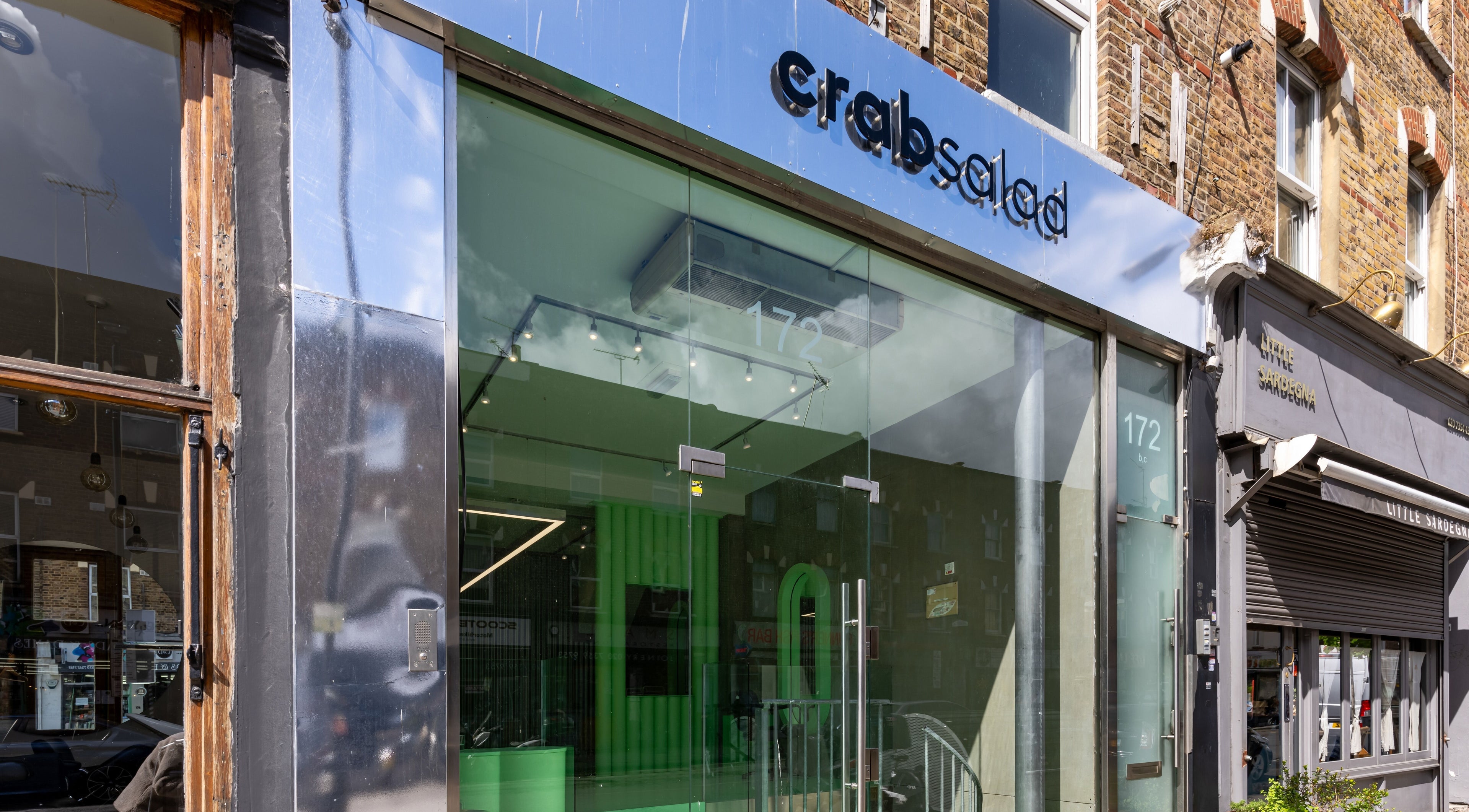 Front view of Crab Salad Highbury in London, GB, showcasing a sleek glass entrance with modern signage.