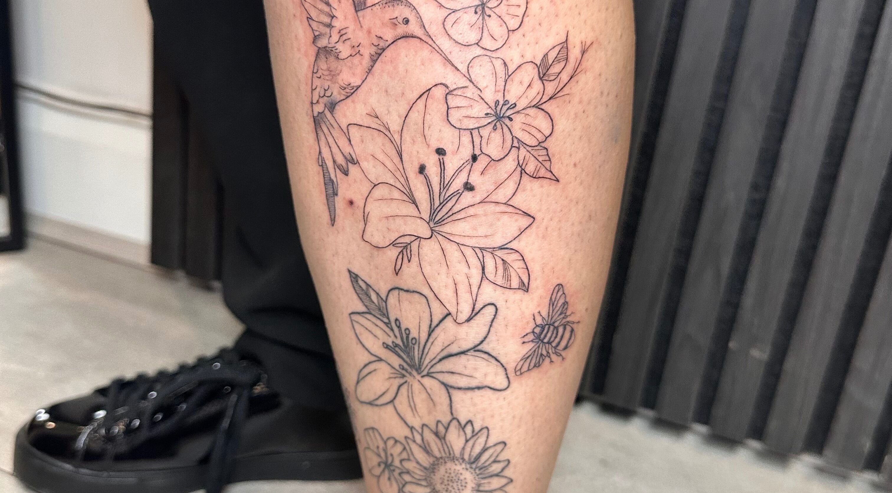 Detailed floral leg tattoo featuring hummingbird at Finelines by Fern Tattoo, Wickford, England, GB.