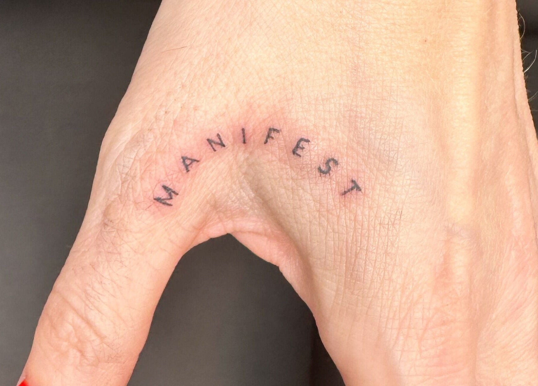 Finelines by Fern Tattoo in Wickford, England, GB showcases a minimalist 'Manifest' tattoo on a hand.