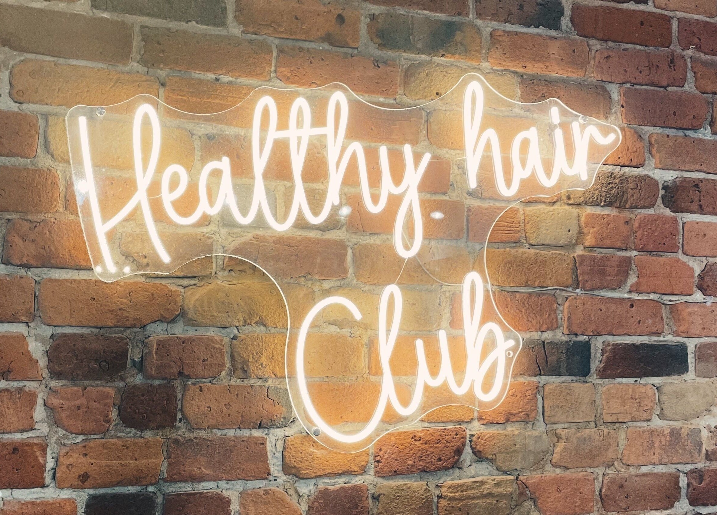 Enseigne néon 'Healthy Hair Club' sur mur de briques chez Teck Studio, Montréal, Québec, CA.