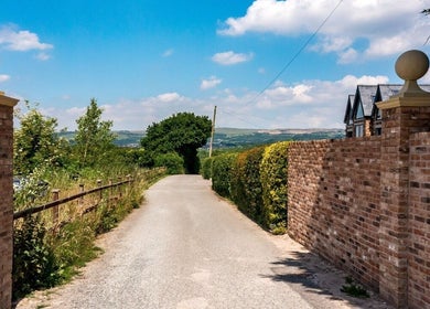 Entrance to Shaped Co. in Westhoughton, England with scenic countryside view and clear blue sky.