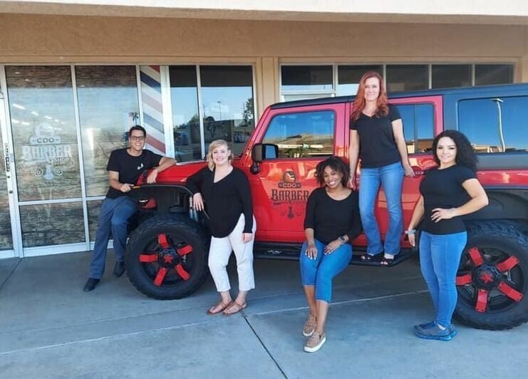 Team at CDO Barbershop in Tucson, Arizona, US posing by red jeep for community event.