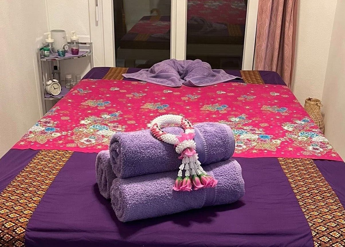 Letto da massaggio all'Ascona Siam Massage Spa, Ascona, Ticino, CH, con asciugamani viola e decorazioni floreali.