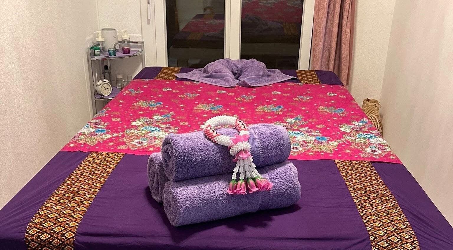 Letto da massaggio all'Ascona Siam Massage Spa, Ascona, Ticino, CH, con asciugamani viola e decorazioni floreali.