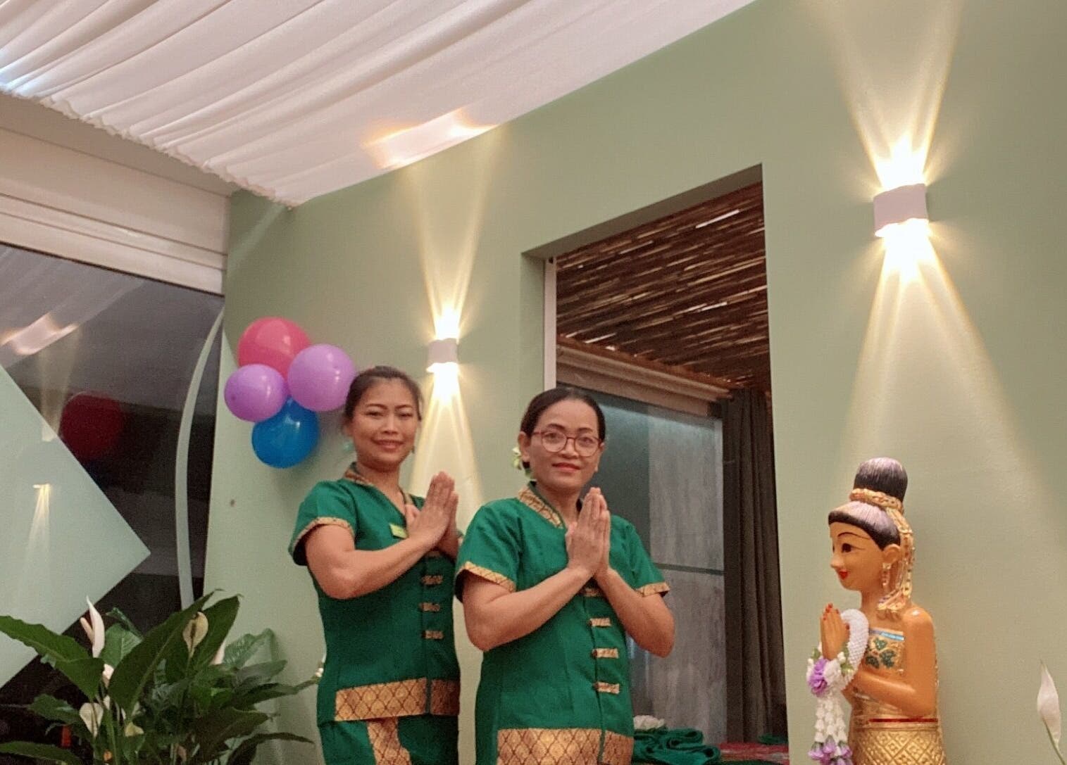 Operatori sorridenti al Locarno Siam Massage di Locarno, Ticino, CH in abiti tradizionali accanto a una statua.