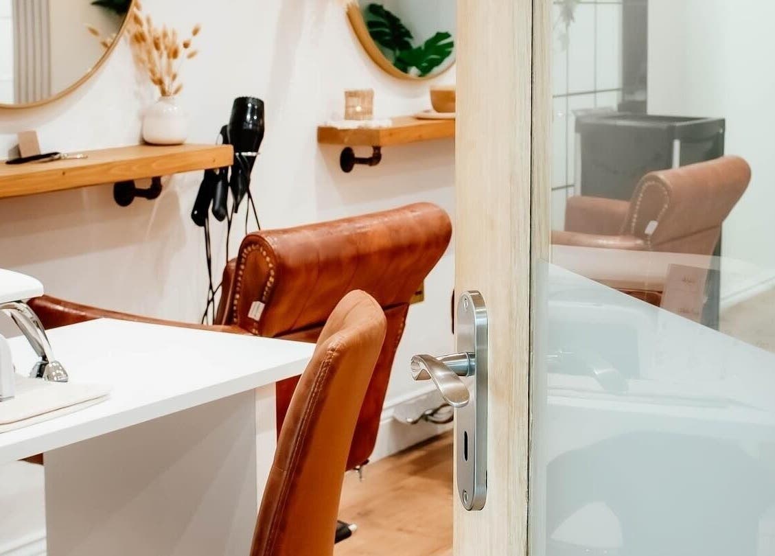 Chic salon interior at Ivy Studios, Ripley, England, GB with leather chairs and mirrors on a wooden shelf.
