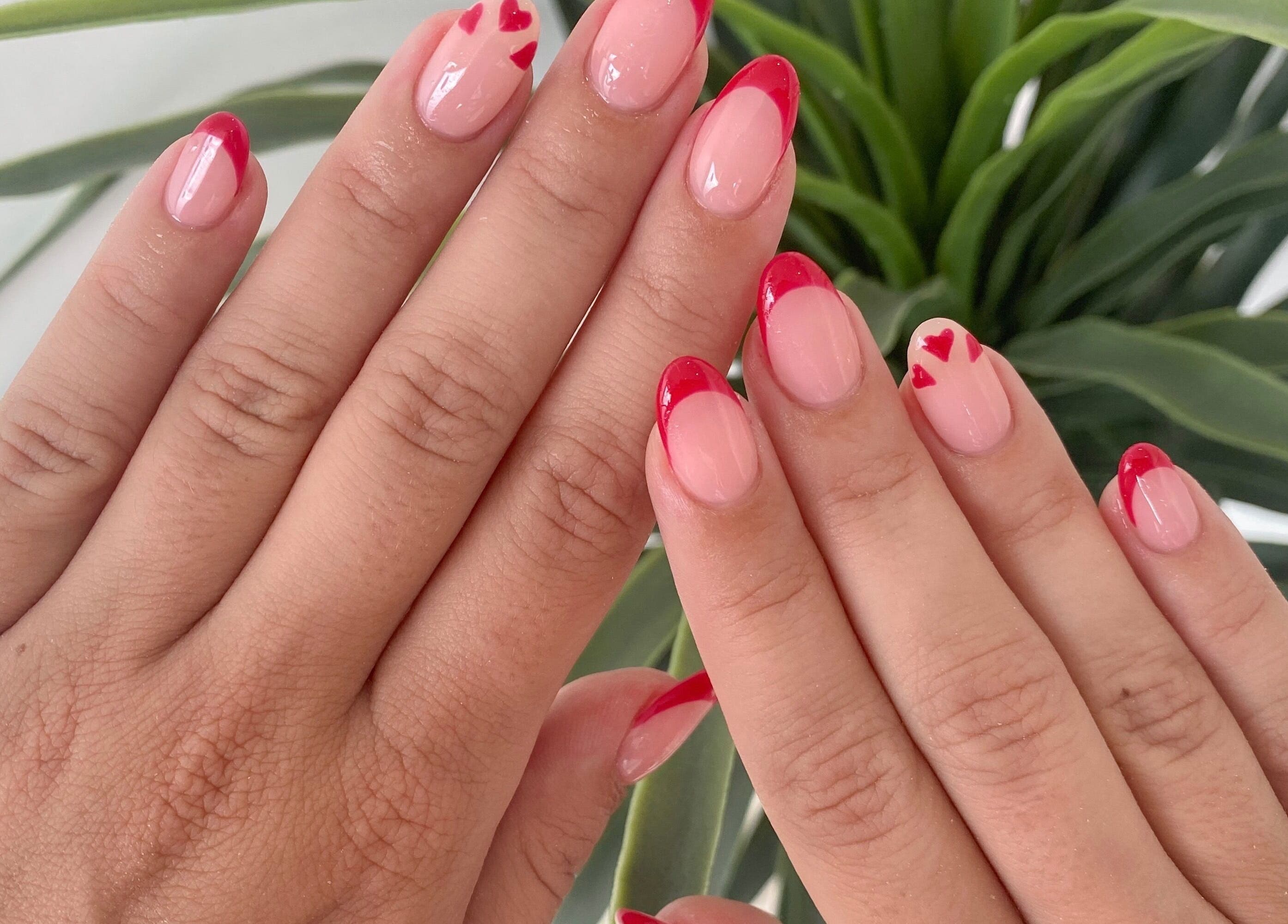 Close-up of red heart tip nails at Jelly Nails in London, England, GB with lush green plant background.