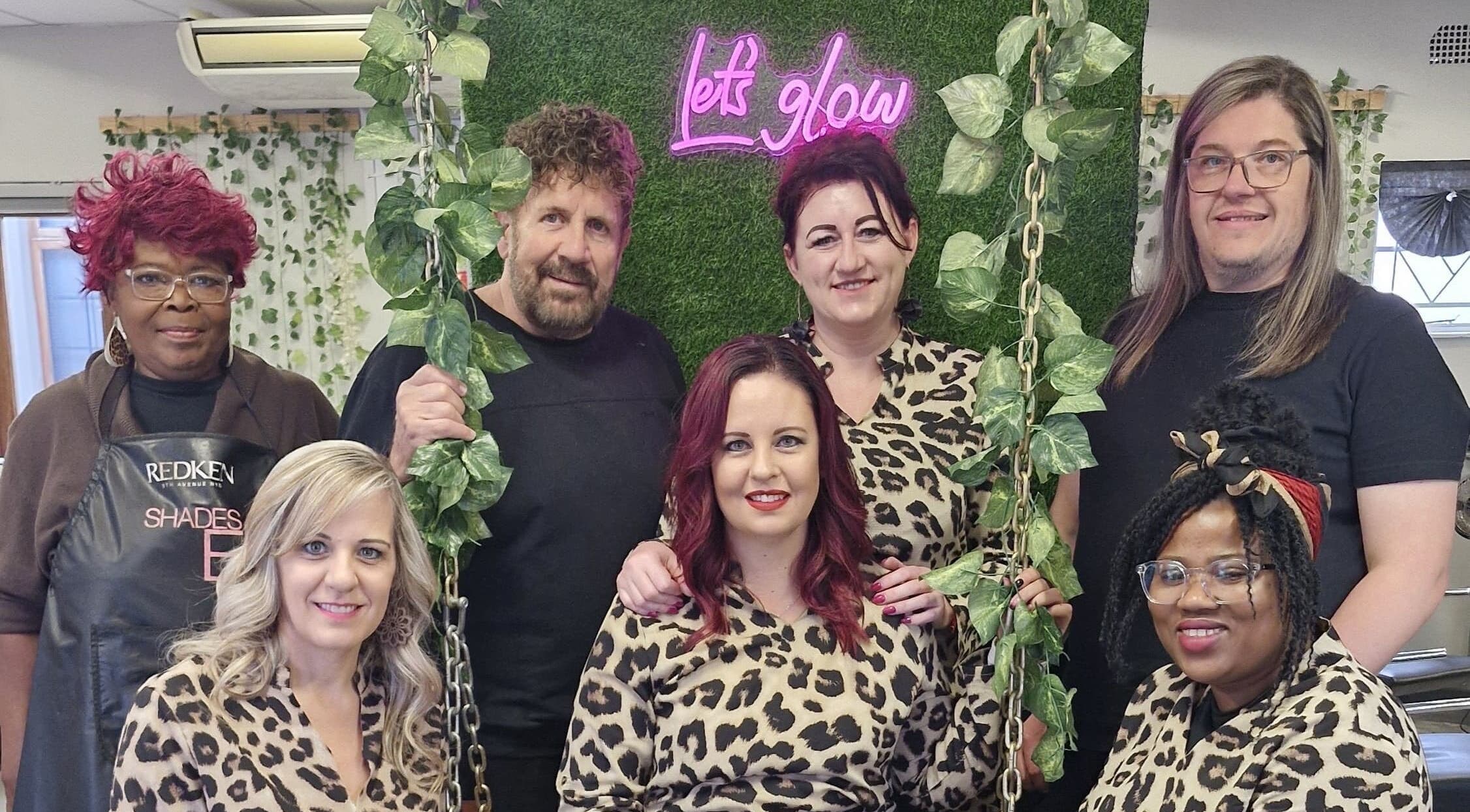 Team of stylists at Xquisite Nails, Bloemfontein, Free State, ZA, in front of a 'Let's Glow' sign.