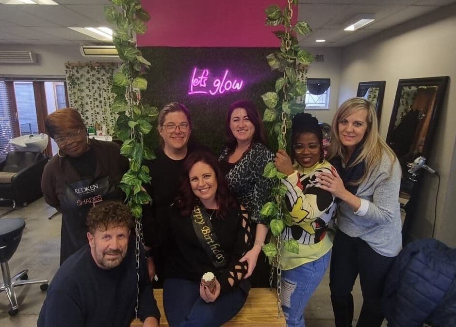 Group of people celebrating at Xquisite Nails in Bloemfontein, Free State, ZA, under 'Let's Glow' sign.