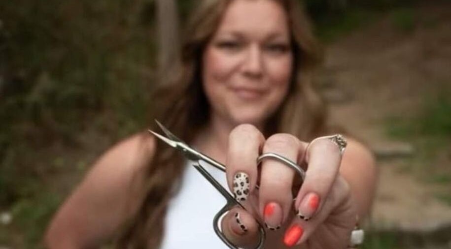 Woman showcasing vibrant nail art with scissors at Hardcorr Nails in Zimmerman, Minnesota, US.