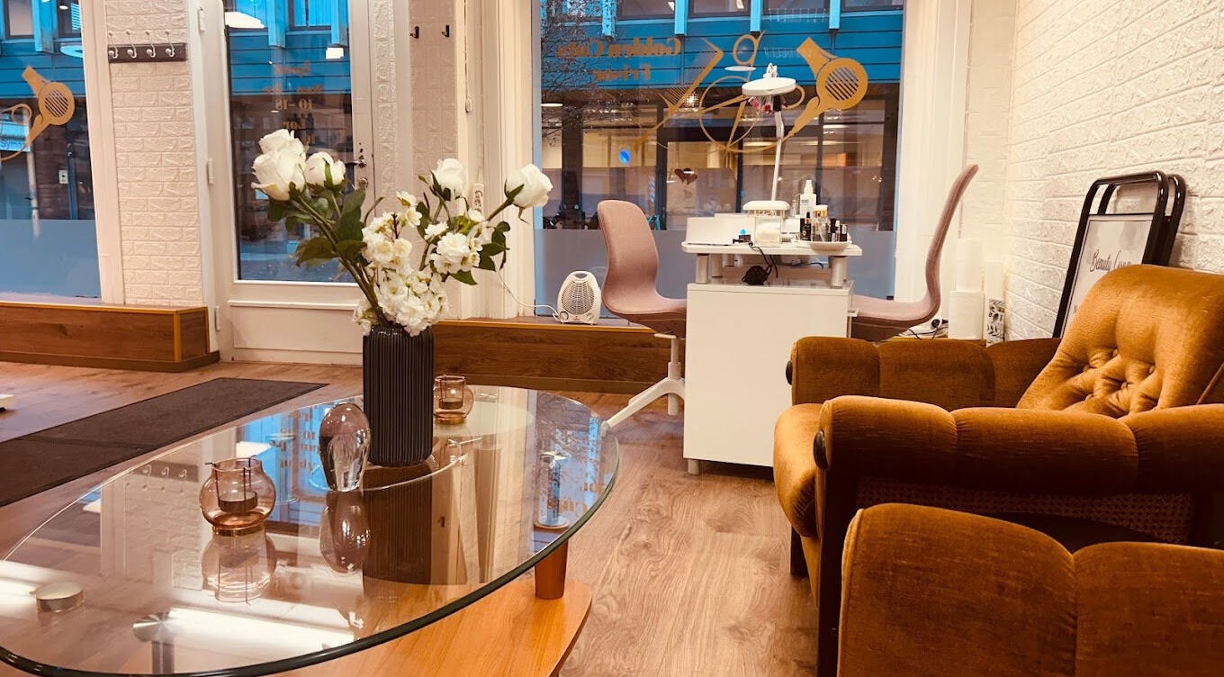 Koselig interiør på Golden Cuts Frisør Sarpsborg, Østfold, NO med sofa, blomster og salongbord.