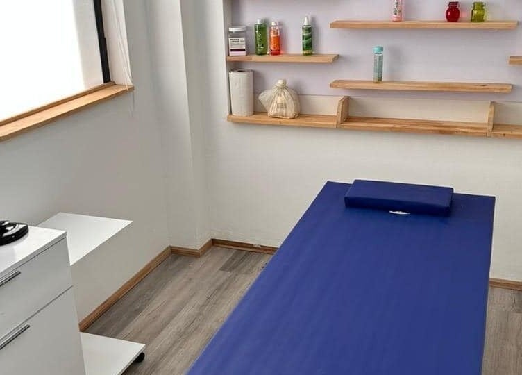 Massage room at Cosmetic Island Port Louis, Port Louis District, MU with a blue table and wooden shelves.