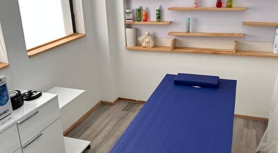 Massage room at Cosmetic Island Port Louis, Port Louis District, MU with a blue table and wooden shelves.
