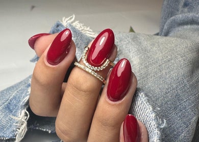 Lux Nails, Galway, showcases vibrant red nails with a gold ring on denim fabric backdrop.