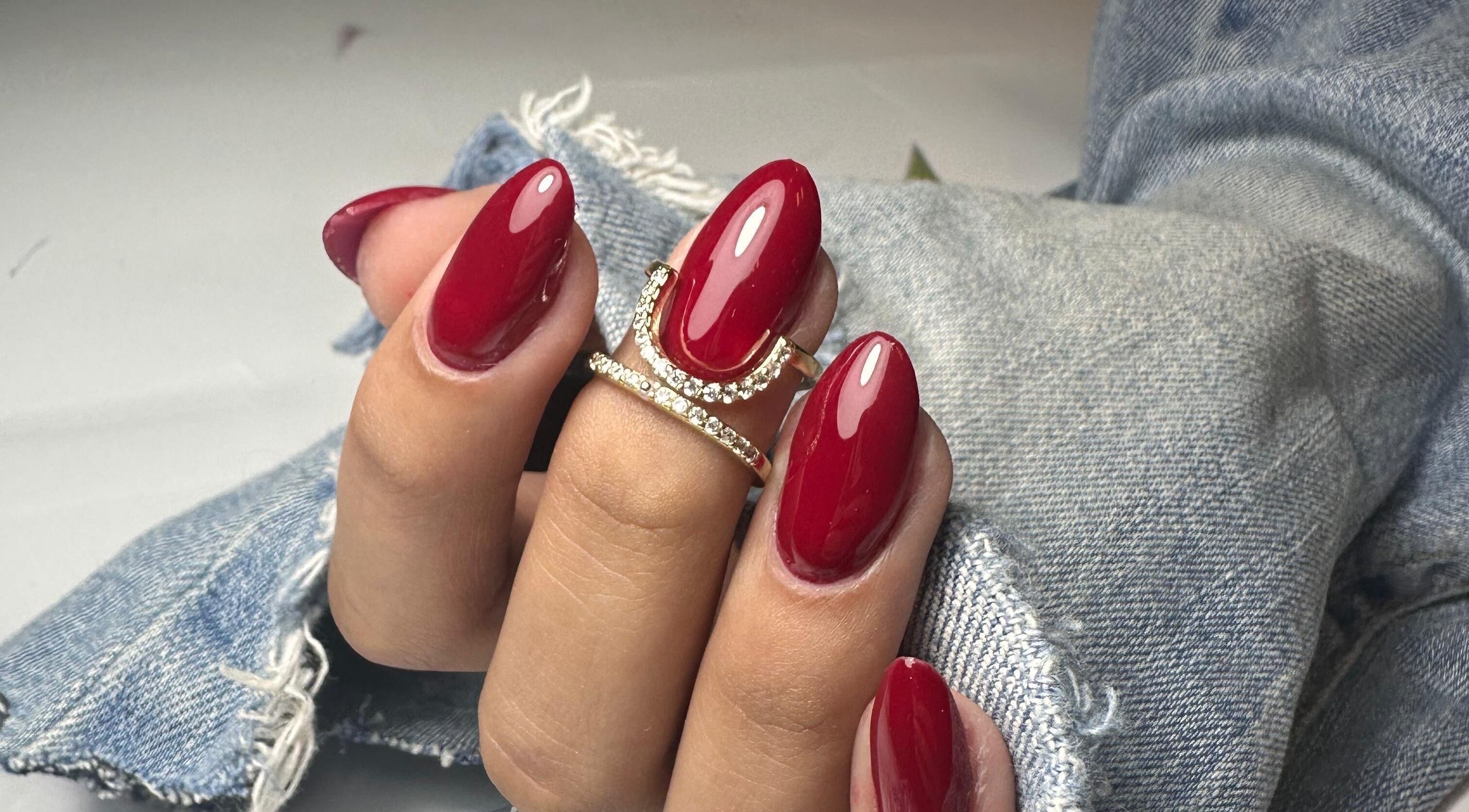 Lux Nails, Galway, showcases vibrant red nails with a gold ring on denim fabric backdrop.