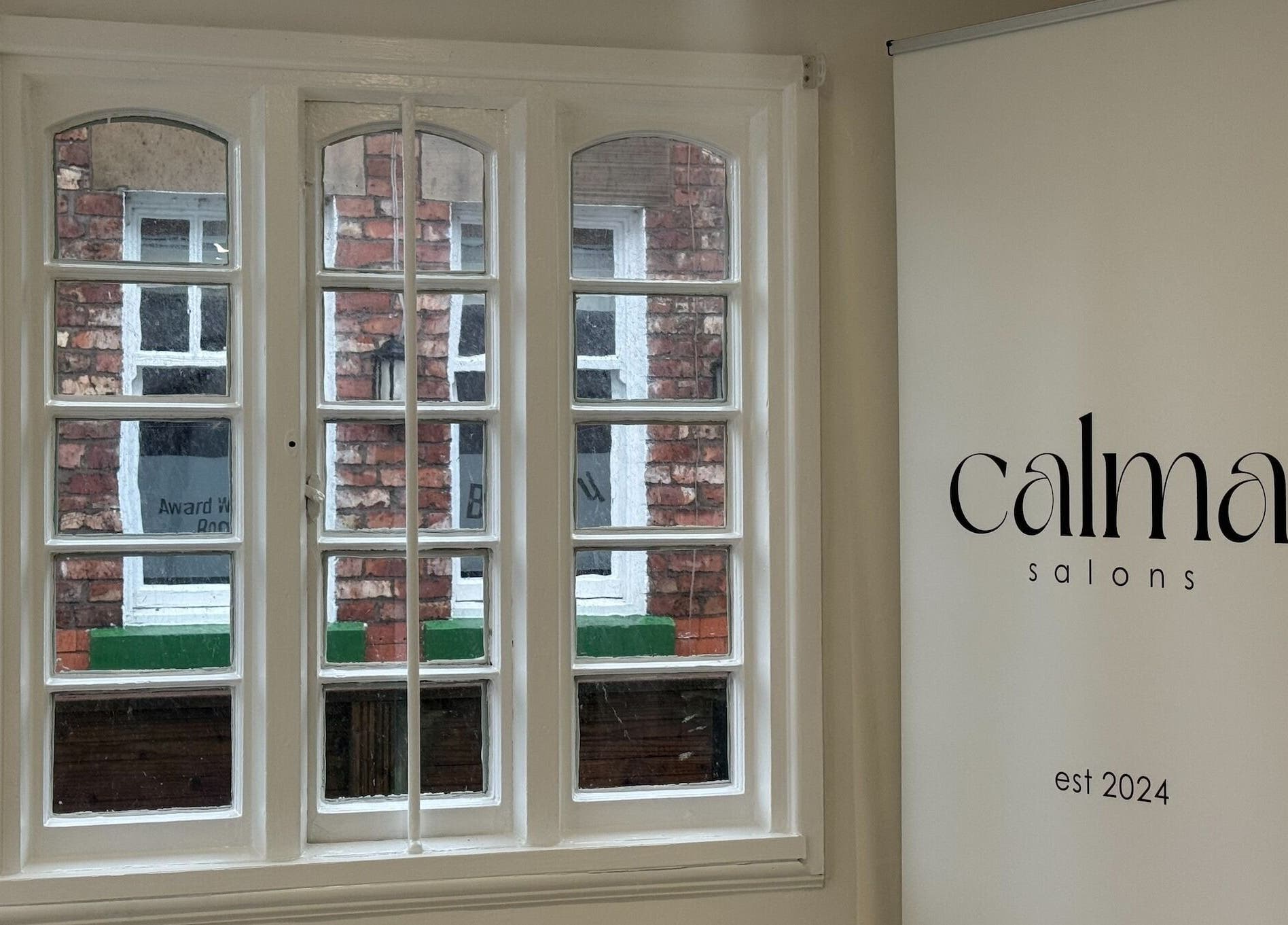 A serene view of Calma Salons - Lymm, England through elegant windows and a branding poster.