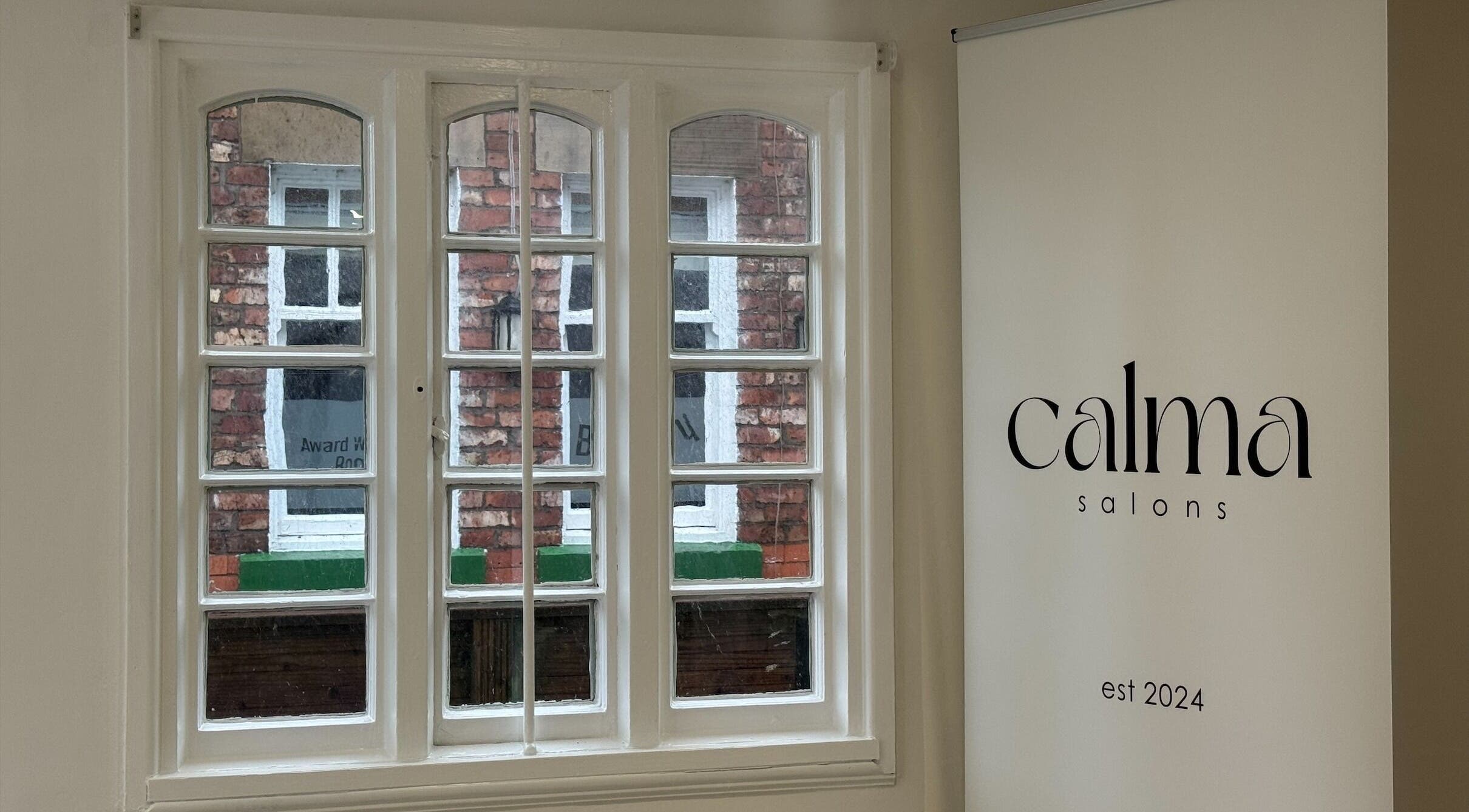 A serene view of Calma Salons - Lymm, England through elegant windows and a branding poster.