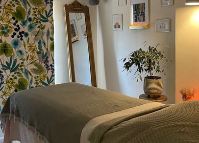 A tranquil therapy room at The Holistic Hideaway, Pott Row, with a floral wall, mirror, and cozy bedding.