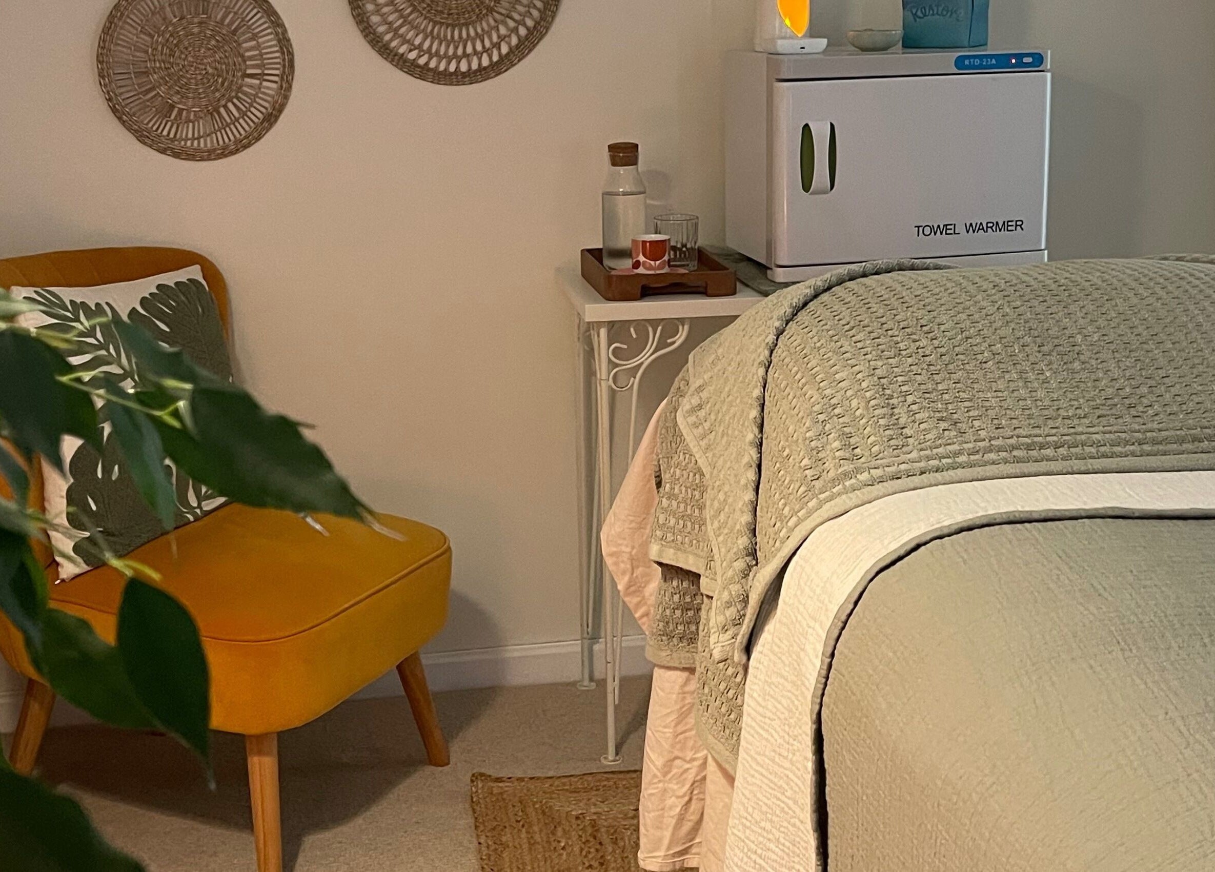 Calm therapy room at The Holistic Hideaway, Pott Row, England, GB, featuring a cozy chair and massage table.